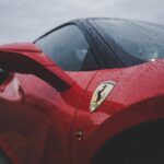 Detailed close-up of a red luxury sports car featuring rain droplets and emblem, evoking speed and elegance.