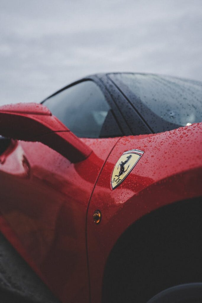 Detailed close-up of a red luxury sports car featuring rain droplets and emblem, evoking speed and elegance.